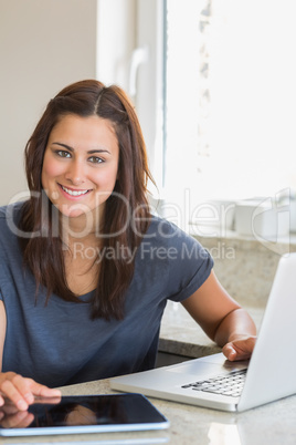 Smiling brunette using the tablet pc and laptop