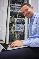 Smiling man using the laptop next to servers