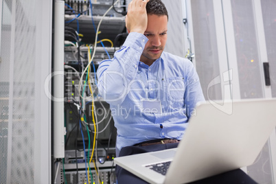 Man getting stressed with laptop over servers