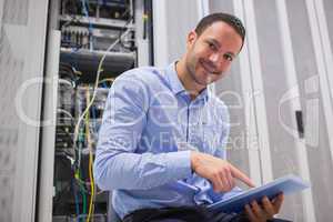 Happy technician working on tablet pc beside servers