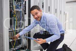 Smiling technician with tablet pc plugging cables into server