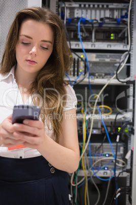 Woman texting on her smartphone in front of servers