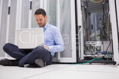Man sitting on floor with laptop beside servers