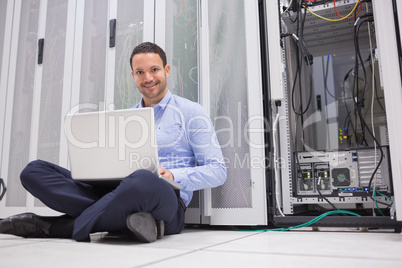 Smiling man sitting on floor checking servers with laptop