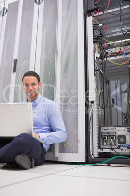 Man sitting on floor using laptop to check servers