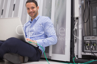 Happy technician working on laptop connected to server