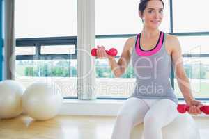 Happy woman lifitng weights on exercise ball
