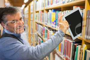 Smiling man taking a tablet pc from shelves
