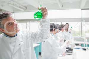 Man viewing liquid while other chemists doing research
