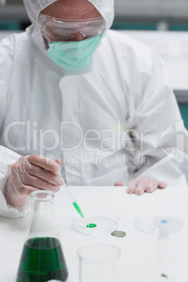 Chemist in protective suit adding green liquid to petri dish