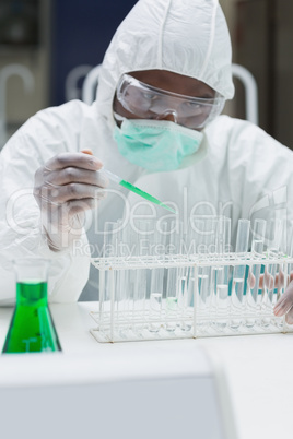 Chemist adding green liquid to test  tubes