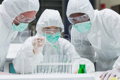 Chemist adding green liquid to test tubes with two other chemist