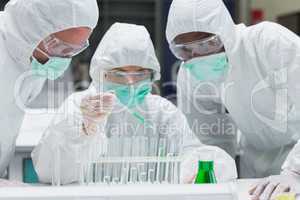 Chemist adding green liquid to test tubes with two other chemist