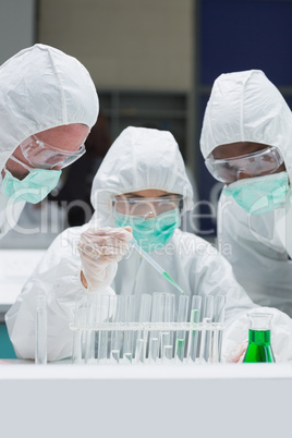 Two chemists watching another adding green liquid to test tubes