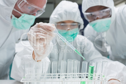 Chemist adding green liquid to test tubes as two others are watc