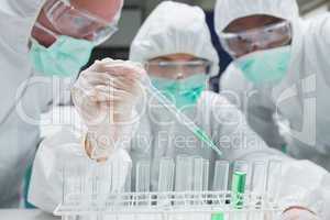 Chemist adding green liquid to test tubes as two others are watc