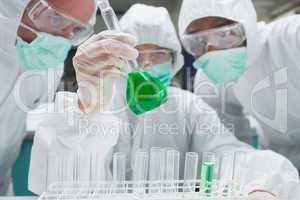 Chemist mixing green liquid in beaker with two chemists watching