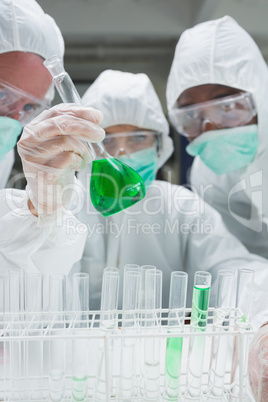 Chemists in protective suits looking at green liquid in beaker