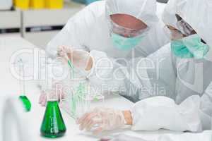 Two chemists adding green liquid to test tubes