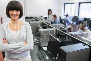 Teacher standing at front of computer class with arms crossed