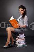 Cute mixed race student girl reading while sitting on heap of bo