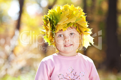 beautiful little girl in a wreath of maple leaves in autumn fore