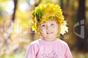 beautiful little girl in a wreath of maple leaves in autumn fore