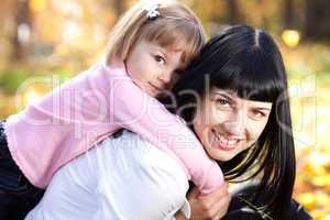 beautiful young mother holding her daughter on back