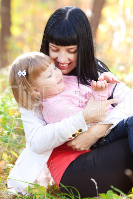 beautiful young mother kissing her daughter in autumn forest