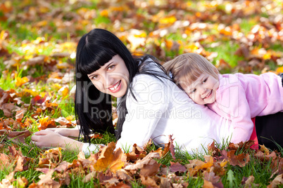 beautiful young mother and her daughter lying on the autumn leav
