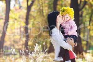 beautiful young mother holding her daughter in a wreath of maple
