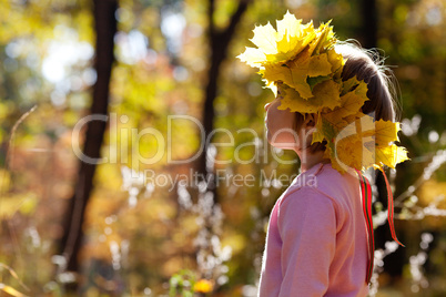 beautiful little girl in a wreath of maple leaves in autumn fore