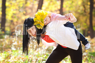 beautiful young mother holding her daughter in a wreath of maple