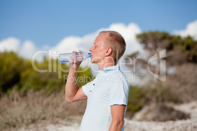 junger mann trinkt wasser am strand auf einer düne im Sommer
