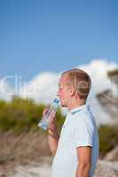 junger mann trinkt wasser am strand auf einer düne im Sommer