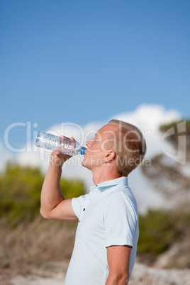 junger mann trinkt wasser am strand auf einer düne im Sommer junger mann trinkt wasser am strand auf einer düne im Sommer