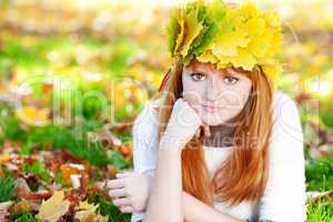 young redhead teenager woman in a wreath of maple leaves lying o