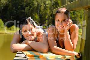 Mother and daughter sunbathing on pier smiling