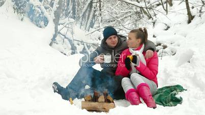 Couple Sitting by Bonfire in Winter Forest