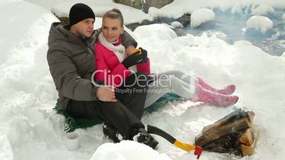 Couple Warming Up by Bonfire in Winter Forest