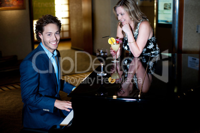 Man playing piano and entertaining his companion holding cocktail