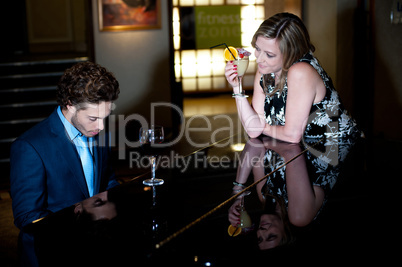 Woman enjoying cocktail and admiring man playing piano