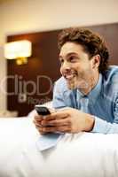 Man holding cellphone and lying on bed, relaxed