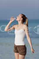 Frau trinkt wasser aus einer flasche am Strand Hochformat