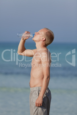 Mann trinkt wasser aus einer flasche am Strand Hochformat