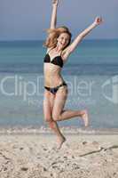 Frau mit Bikini springt fröhlich am Strand Hochformat