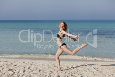 Frau mit Bikini springt fröhlich am Strand Querformat