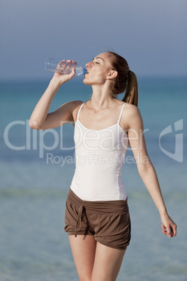 Frau trinkt wasser aus einer flasche am Strand Hochformat