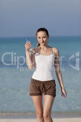 Frau trinkt wasser aus einer flasche am Strand Hochformat