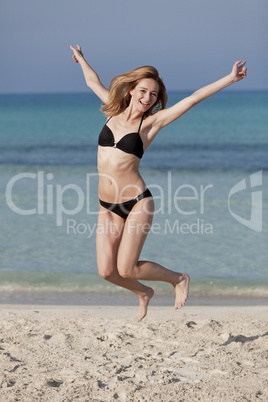 Frau mit Bikini springt fröhlich am Strand Hochformat